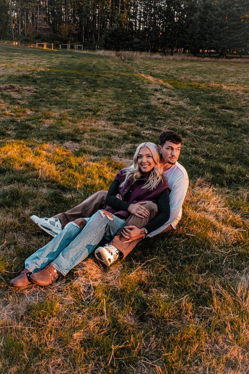 Engaged couple cuddled together in a golden-hour field