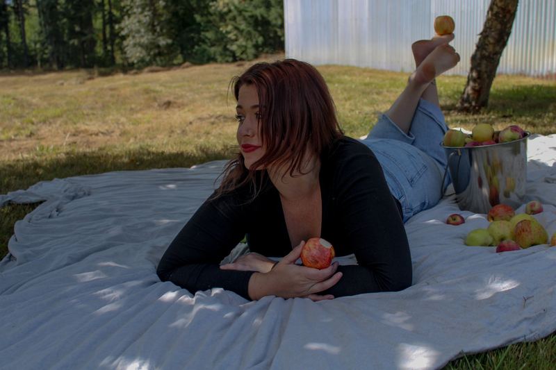 Young woman with red hair lying on a picnic blanket holding a peach