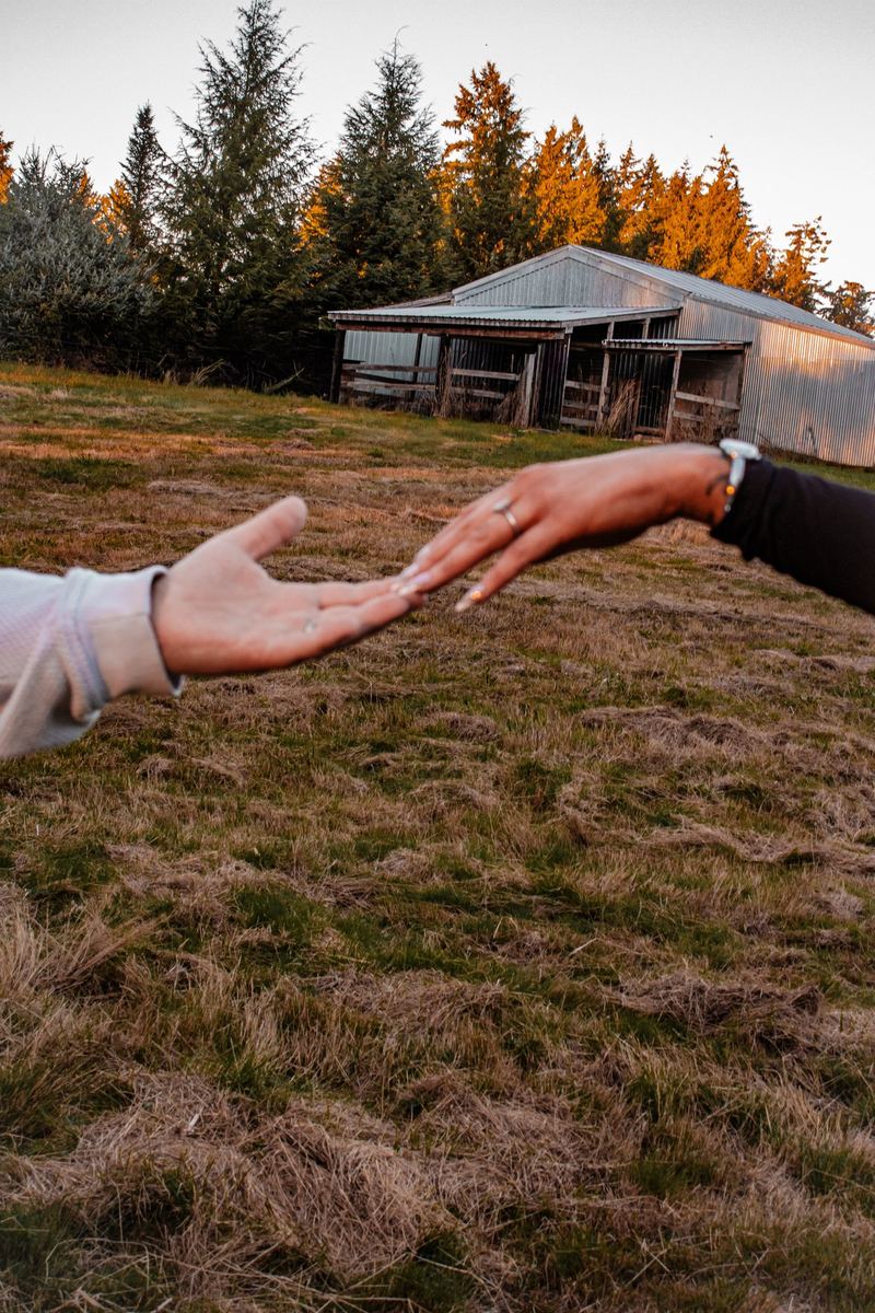 Couple reaching for each other's hands, engagement ring in view, barn behind