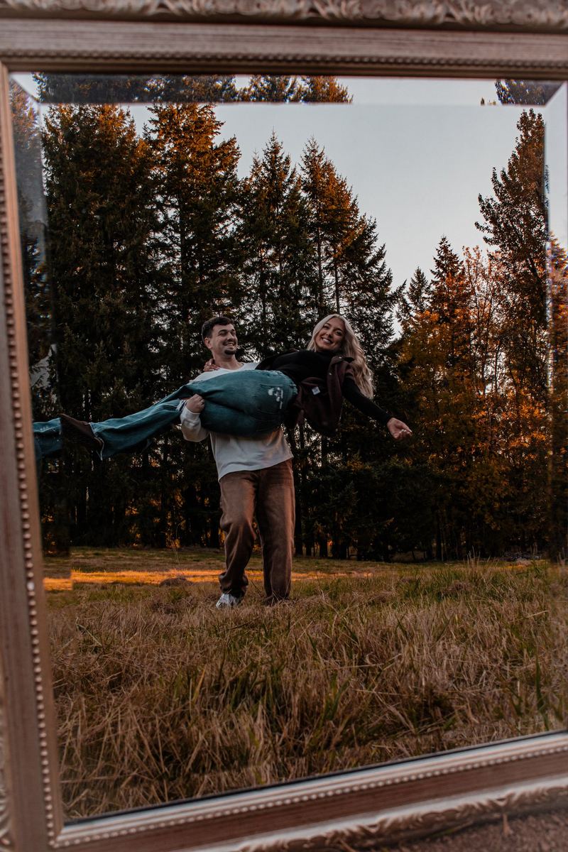 Man lifting his fiancée, framed in an antique mirror in a field